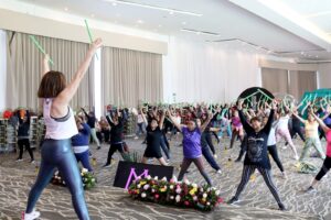 Mujeres participantes disfrutan de la clase de Pound, guiada por la entrenadora Gaby Cuevas, como parte del evento 