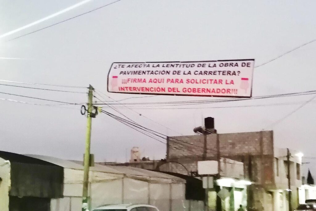 En diciembre de 2025, vecinos colocaron una manta con la leyenda: “¿Te afecta la lentitud de la obra de pavimentación de la carretera? Firma aquí 
