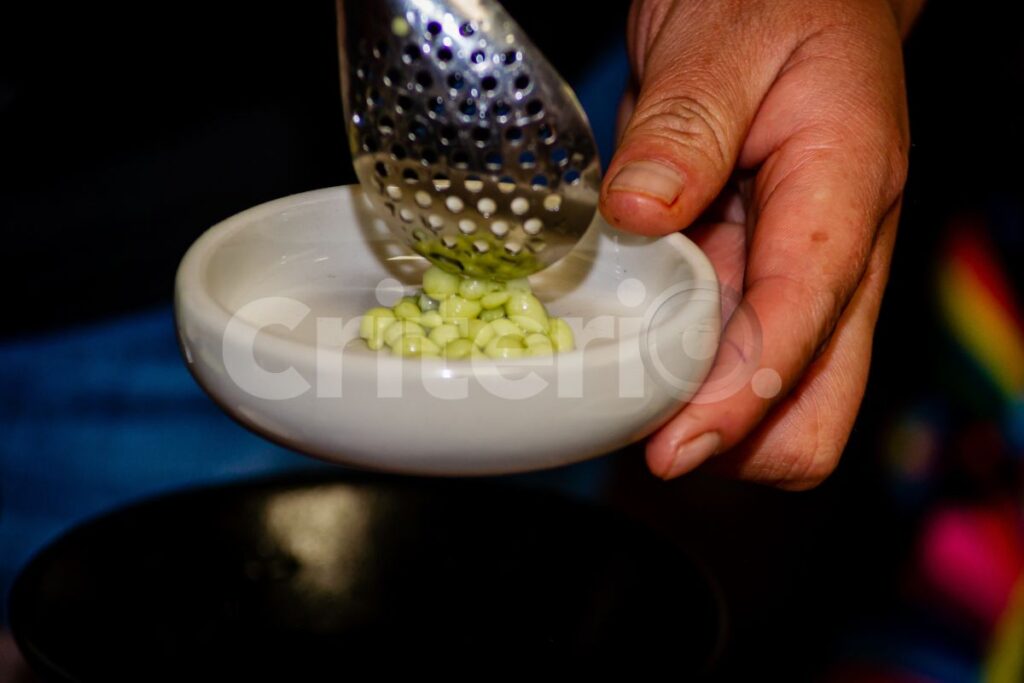 Una mano sirve con una cuchara perforada varias cápsulas de sabor en un tazón